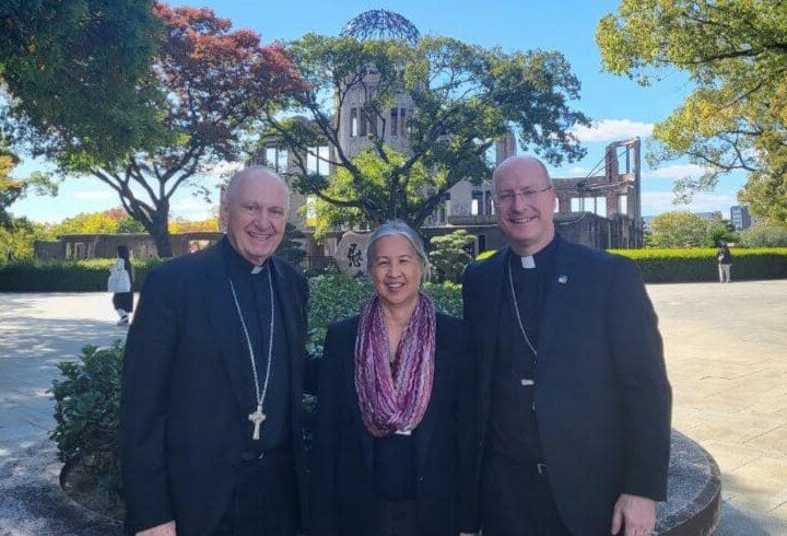 Bishop Richard Pates, administrator of the Diocese of Dubuque, Iowa; Virginia Farris, USCCB foreign policy advisor to the U.S. Conference of Catholic Bishops; and Bishop W. Shawn McKnight stand together near the Genbaku Dome, which is part of the Hiroshima Peace Memorial Park in Hiroshima, Japan. This was the only structure left standing in the area where the first atomic bomb exploded on Aug. 6, 1945. The ruins have been preserved and serve as a symbol of hope for world peace.